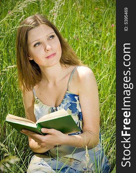 Cute young romantic girl reading an interesting book, sitting in tall grass. Cute young romantic girl reading an interesting book, sitting in tall grass