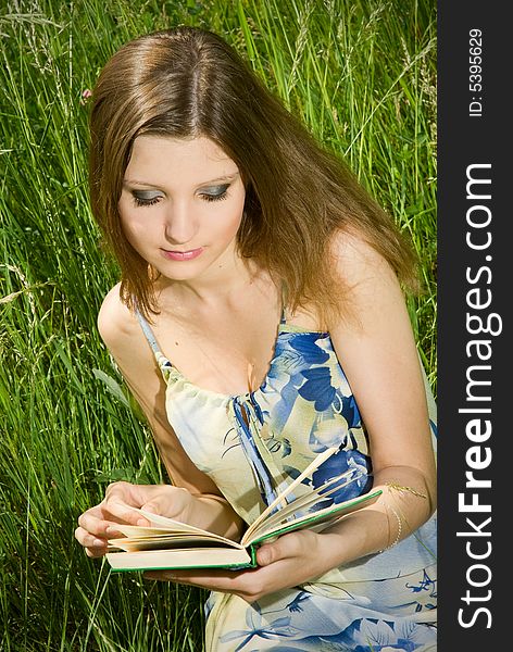 Cute young romantic girl reading an interesting book, sitting in tall grass. Cute young romantic girl reading an interesting book, sitting in tall grass