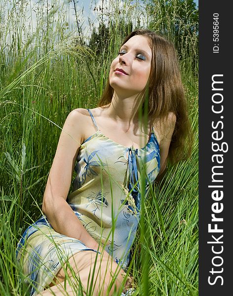 Young romantic girl sitting in tall grass, enjoying the sun