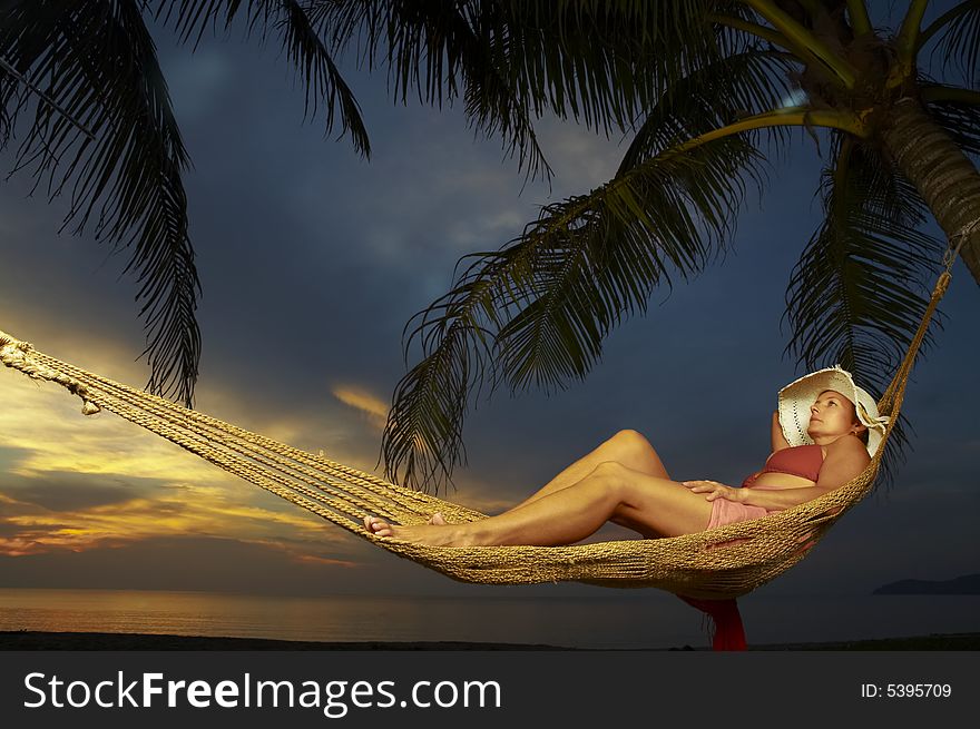 View of a woman lounging in hammock during sunset. View of a woman lounging in hammock during sunset