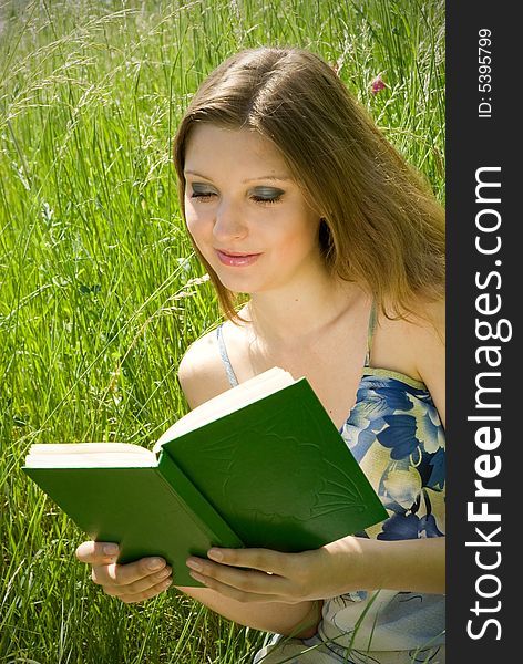 Cute young romantic girl reading an interesting book, sitting in tall grass. Cute young romantic girl reading an interesting book, sitting in tall grass