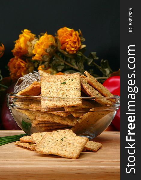 Square sour cream and chive flavored crackers in glass bowl on cutting board in kitchen or restaurant.
