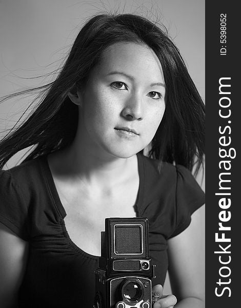 Black and white image of a young Asian woman taking a photograph with a medium format twin lens camera.