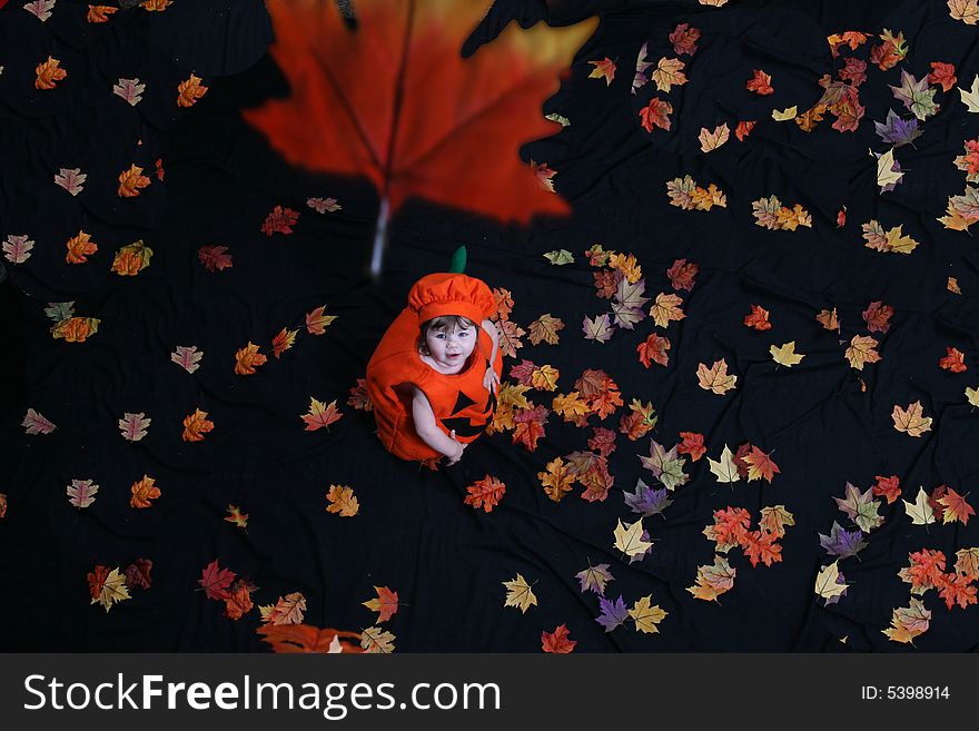 Pretty little girl dressed in a pumpkin costume, watching leaves fall from above; shot from above. Pretty little girl dressed in a pumpkin costume, watching leaves fall from above; shot from above.