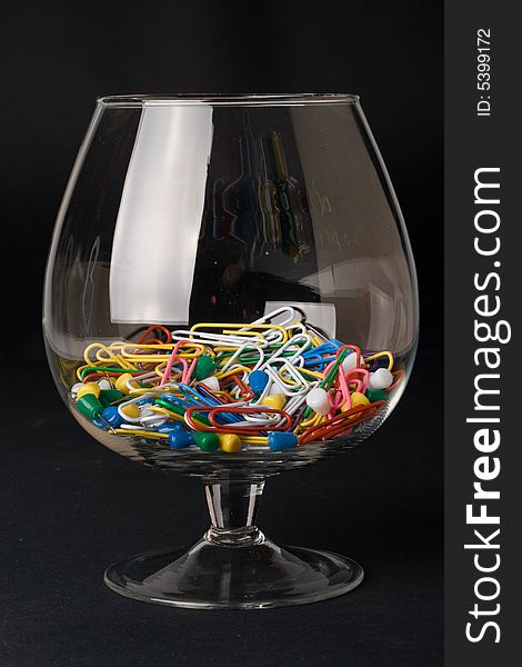 Colored paperclips and pins in a glass on a black background. Close up. Selective focus.