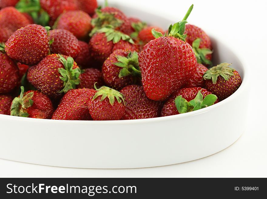 Some fresh strawberries in white bowl; white background