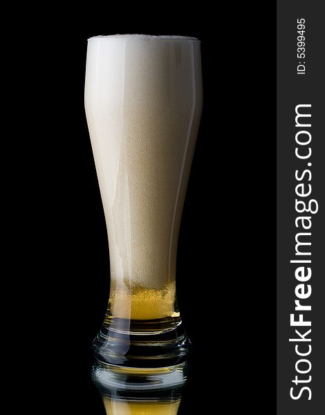 Fresh foamy beer in a glass on a black background.