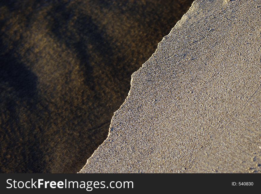 A small stream cuts through an area of flat sand in low sun. A small stream cuts through an area of flat sand in low sun