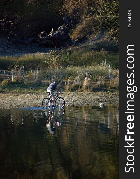 A man riding a bicycle by a pond. A man riding a bicycle by a pond