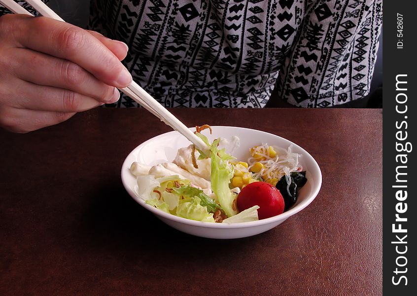 Girl eating salad with chopsticks at a restaurant table