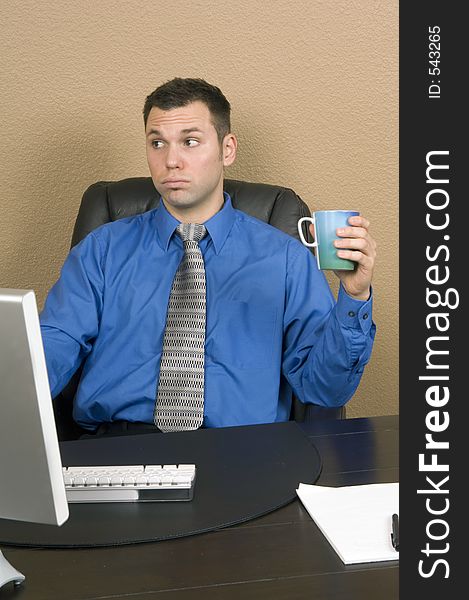 Young male office worker drinking his coffee at his computer with serious things on his mind. Young male office worker drinking his coffee at his computer with serious things on his mind