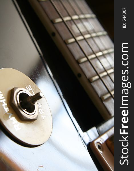 Image of the fret board and rythm and treble toggle on an old fashioned black glossy guitar. Image of the fret board and rythm and treble toggle on an old fashioned black glossy guitar