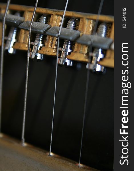 Close up image of the strings and nuts on an old fashioned black electric guitar - extreme mechanical close up. Close up image of the strings and nuts on an old fashioned black electric guitar - extreme mechanical close up