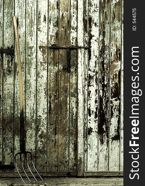 A fork tool in front of an old painted wooden farm door, toned. A fork tool in front of an old painted wooden farm door, toned.