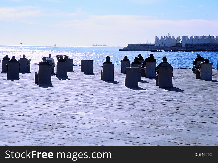 People relaxing on the waterfront on stone chairs. one could imagine that people were waiting for some kind of space ship to arrive for boarding. People relaxing on the waterfront on stone chairs. one could imagine that people were waiting for some kind of space ship to arrive for boarding