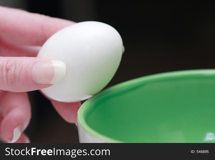 Hand holding an egg over green bowl