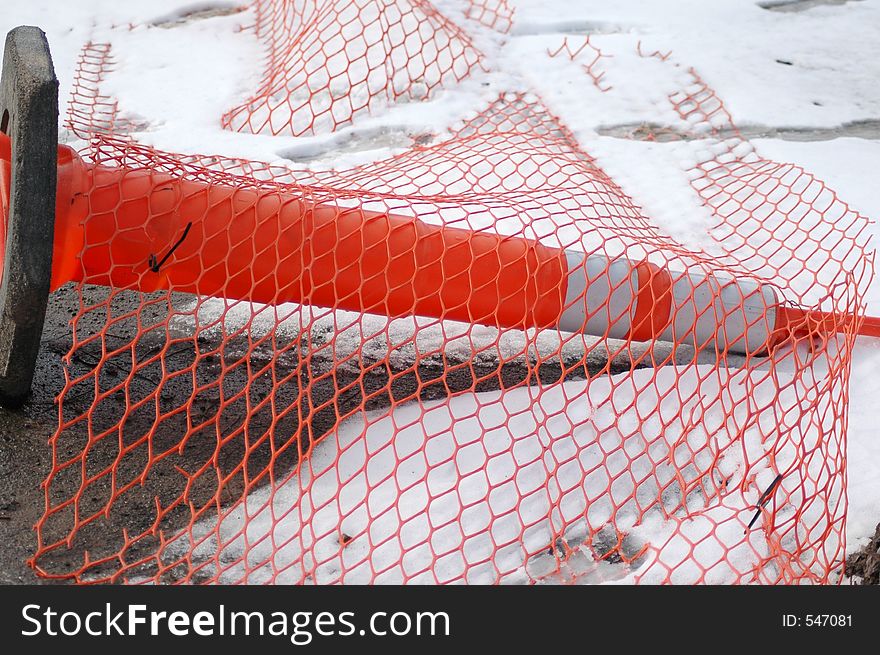 Orange construction cone tipped over with orange coated fencing ove it.