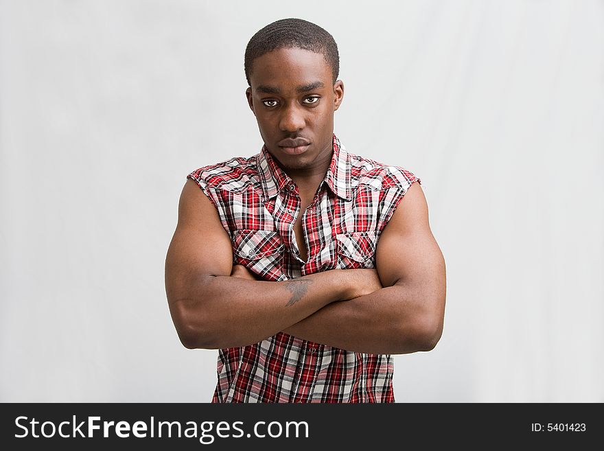 Young dark skinned handsome guy standing like a macho with both arms crossed wearing a checkerd shirt without sleeves. Young dark skinned handsome guy standing like a macho with both arms crossed wearing a checkerd shirt without sleeves.