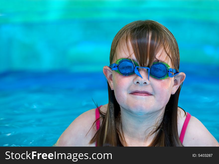 A young girl with swimming goggles in an inflatable pool with space on left for type