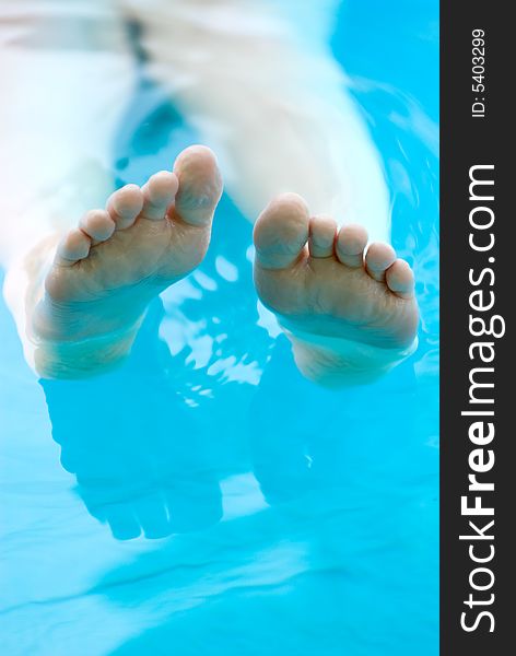 Feet lounging in a pool with space on the right for type