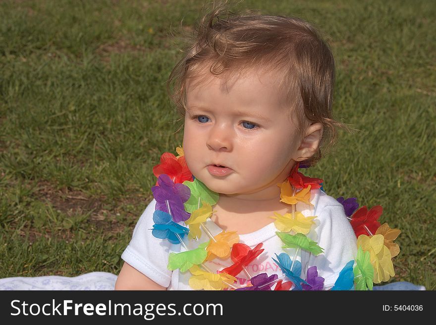 8 months old girl with colorful flowers around the neck sitting on a grass. 8 months old girl with colorful flowers around the neck sitting on a grass