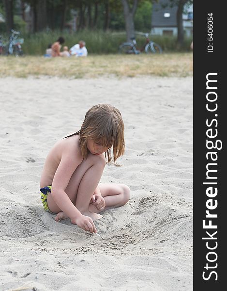 A little girl is drawing on a beach by a lake. A little girl is drawing on a beach by a lake.