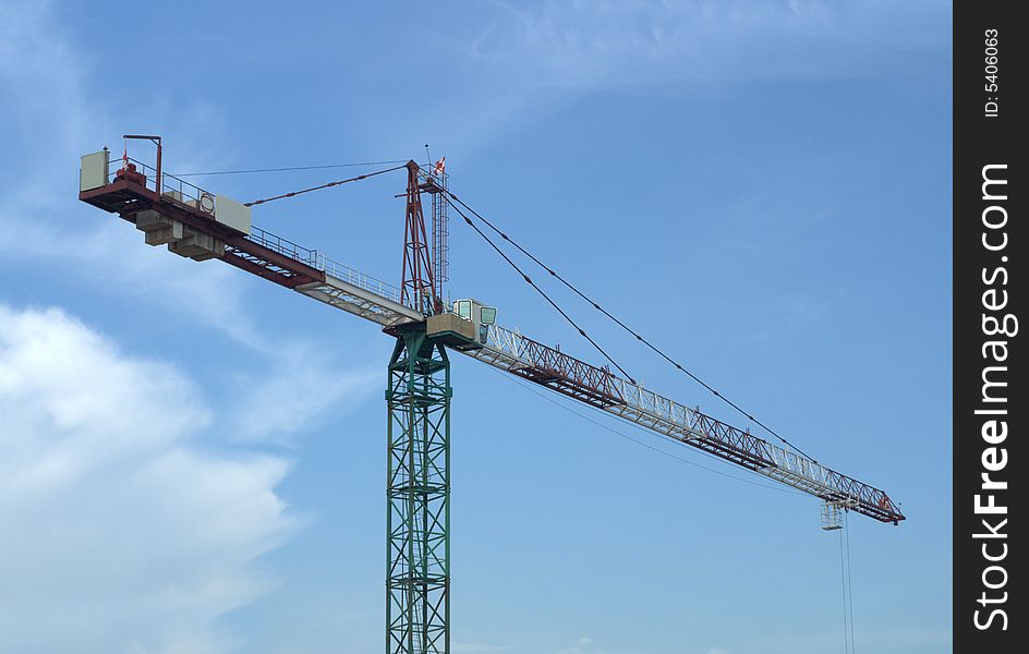 A working tower crane with blue sky and white clouds.