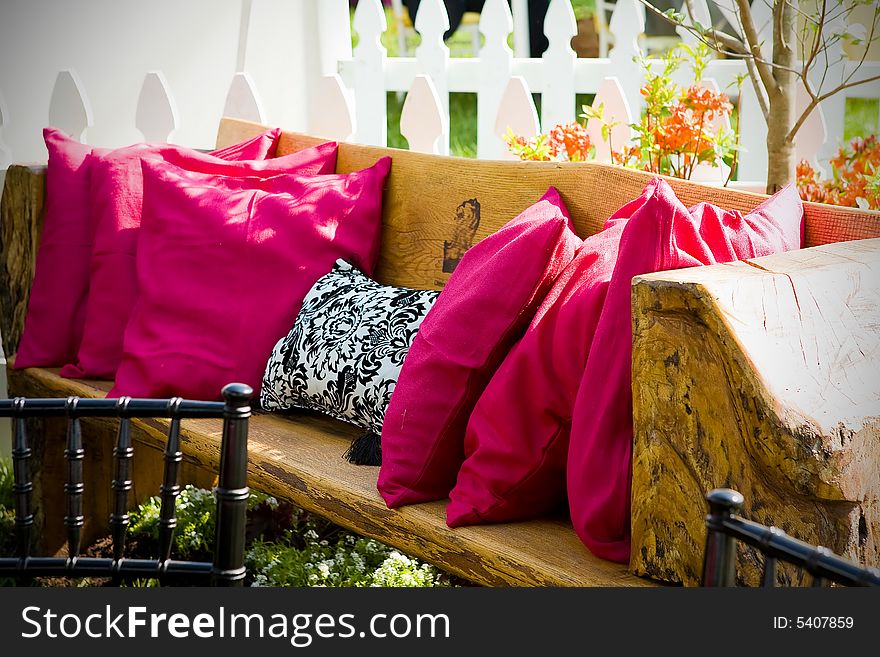 An outdoor wooden bench with red throw pillows