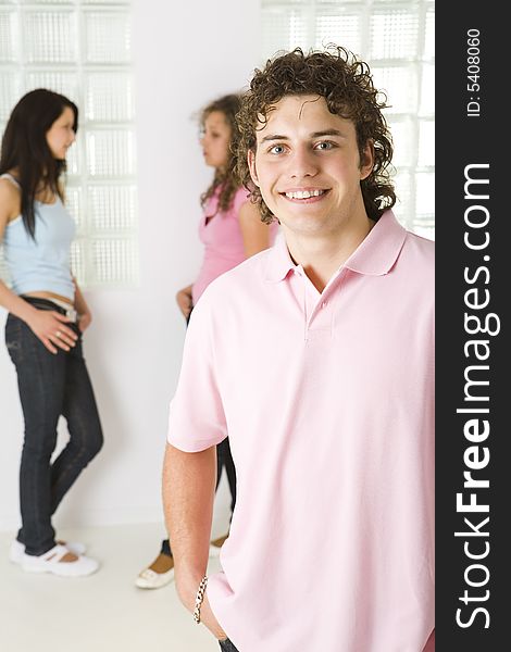 Three friends standing near window. A girls talking with themselves. A boy smiling and looking at camera. Focused on a boy. Three friends standing near window. A girls talking with themselves. A boy smiling and looking at camera. Focused on a boy.