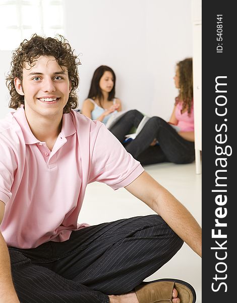 Three friends sitting on the floor. A girls talking with themselves. A boy smiling and looking at camera. Focused on a boy. Three friends sitting on the floor. A girls talking with themselves. A boy smiling and looking at camera. Focused on a boy.