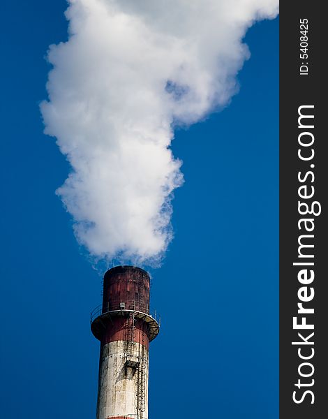 A cooling chimney pumping out white smoke against a blue sky background. A cooling chimney pumping out white smoke against a blue sky background