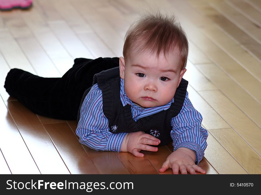 A baby boy dressed in a shirt and vest for the holidays crawling on the hardwood floor. A baby boy dressed in a shirt and vest for the holidays crawling on the hardwood floor