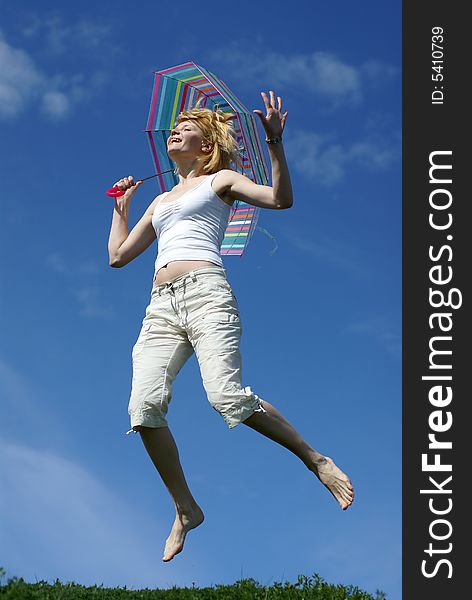 Young jumping charming girl with umbrella against blue sky