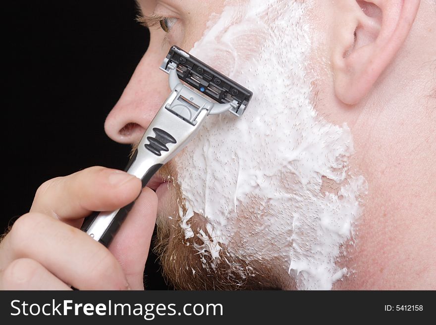 A young man shaves the side of his face to clean up his goatee. A young man shaves the side of his face to clean up his goatee.