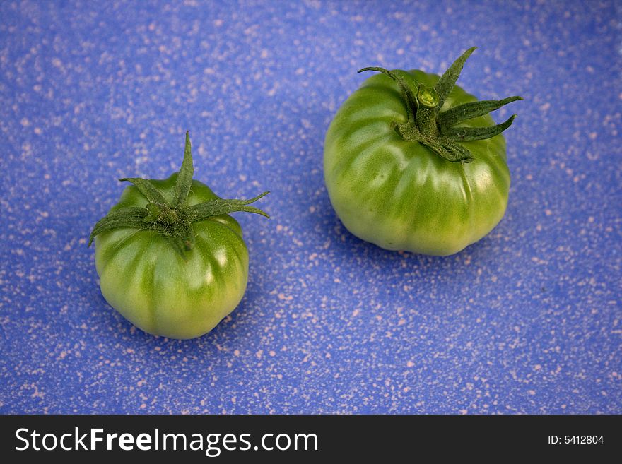 Two green tomatoes on blue tile. Two green tomatoes on blue tile