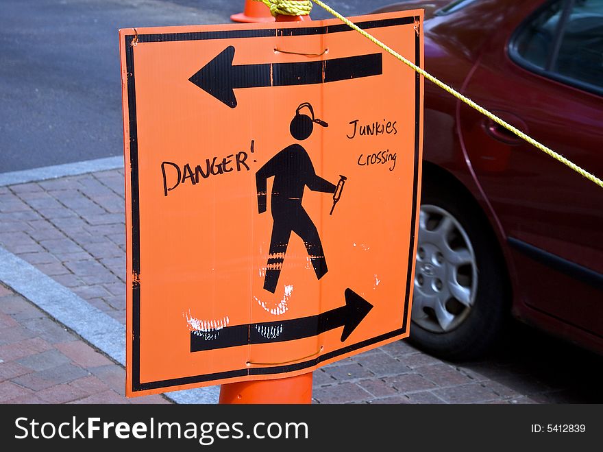 Orange pedestrian sign with arrows stating danger junkies crossing