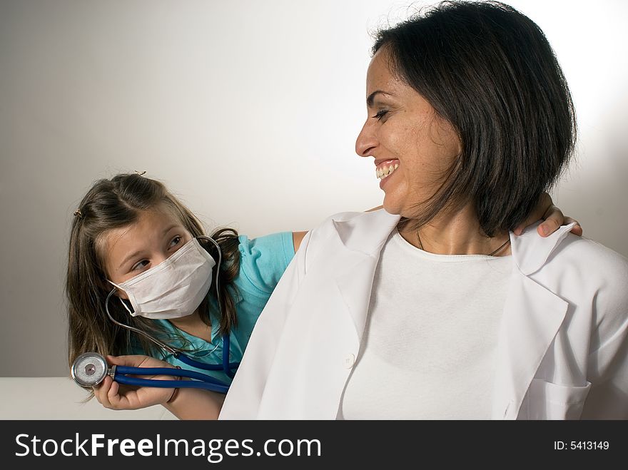 Young girl wearing a mask listens to the smiling doctor's heartbeat. They are having fun and being playful. Horizontally framed photograph. Young girl wearing a mask listens to the smiling doctor's heartbeat. They are having fun and being playful. Horizontally framed photograph