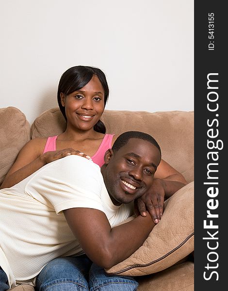 Happy, attractive couple share a couch. Both are smiling and he is lying across her lap. Vertically framed photograph. Happy, attractive couple share a couch. Both are smiling and he is lying across her lap. Vertically framed photograph.