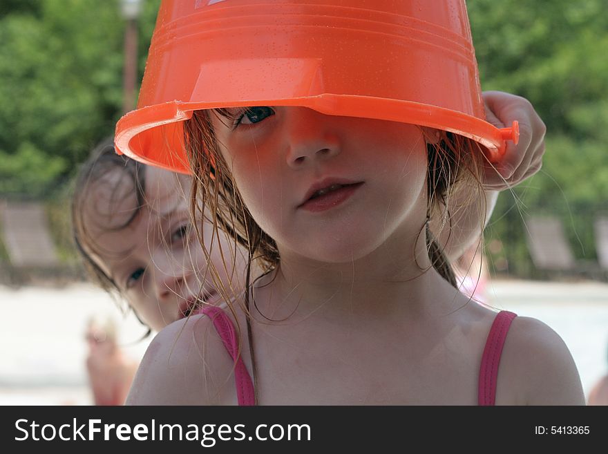 A little girl at the pool with a bucket over her head. A little girl at the pool with a bucket over her head