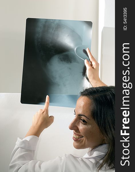 Smiling female doctor points to an x-ray she is holding up. Vertically framed photograph. Smiling female doctor points to an x-ray she is holding up. Vertically framed photograph