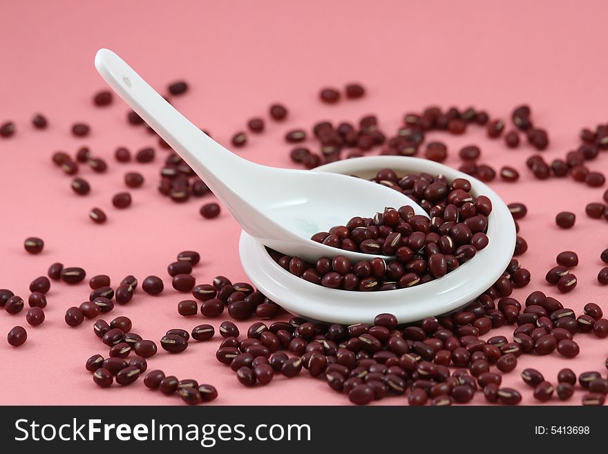 Beans in the spoon and cup on pink background