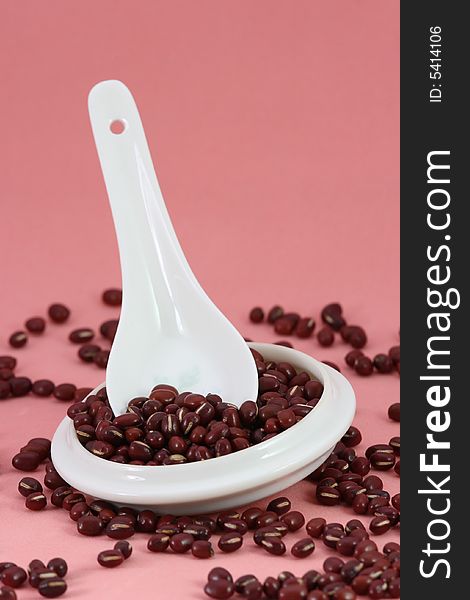 Beans in the spoon and cup on pink background