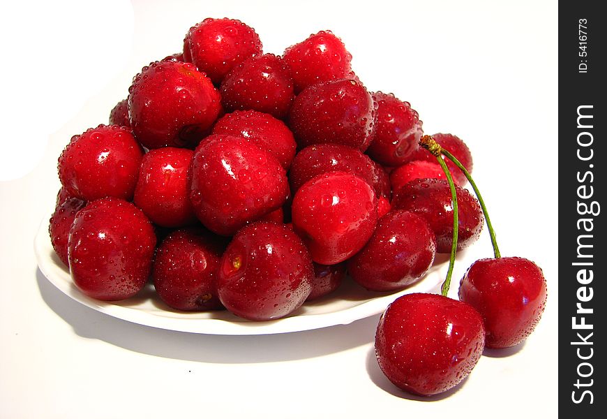 A saucer full of ripe cherry with a coupled berries on the right. A saucer full of ripe cherry with a coupled berries on the right