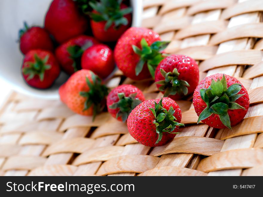 Fresh strawberrys on a woven platter spilling from a white bowl