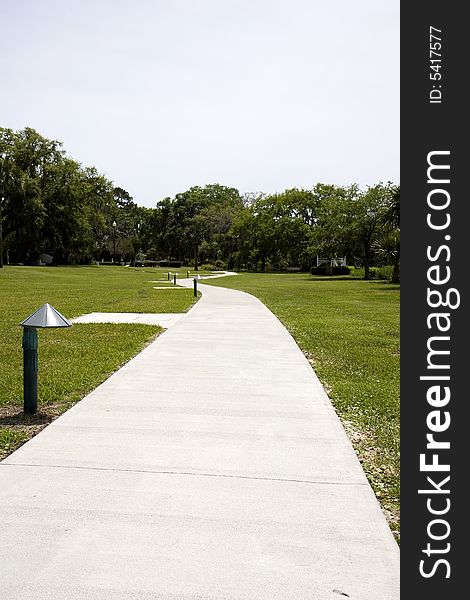 A sidewalk through the grass leading into the trees. A sidewalk through the grass leading into the trees