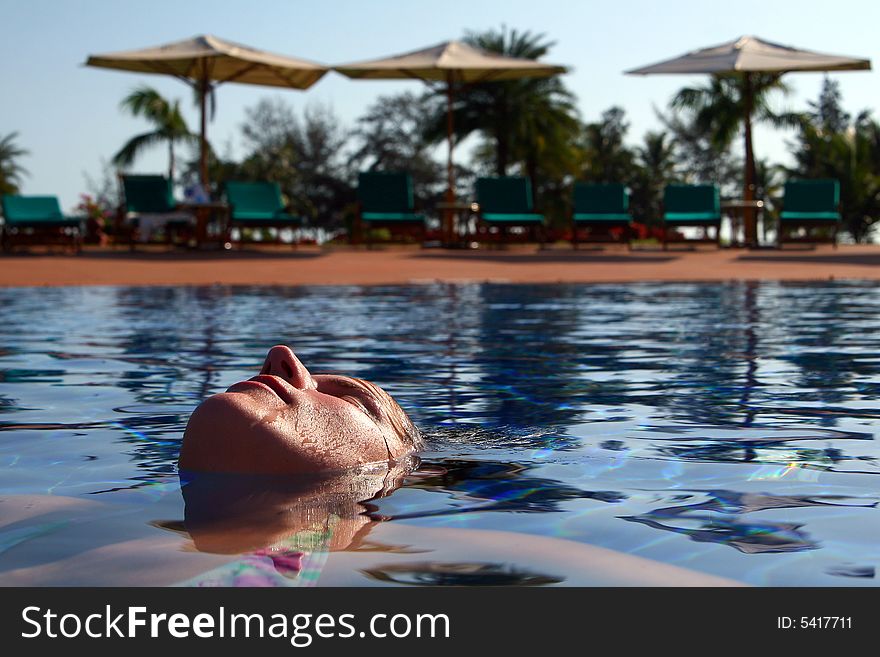 A young woman is relaxing in the pool. Ideal vacation shot with sun umbrellas and palm trees in the back. A young woman is relaxing in the pool. Ideal vacation shot with sun umbrellas and palm trees in the back.