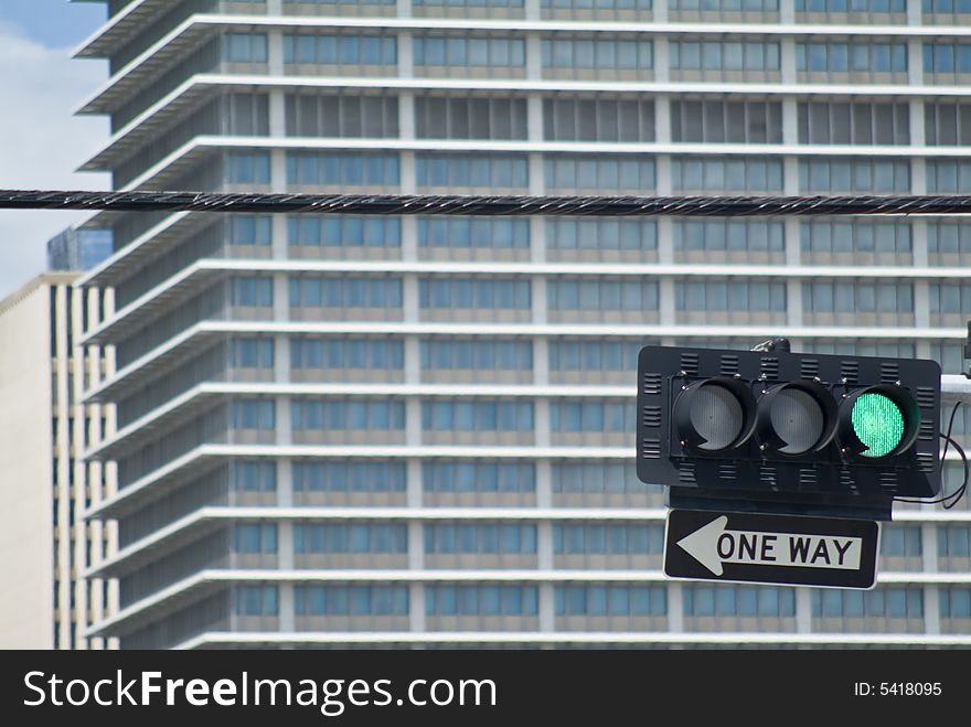 A traffic light on green with one way sign below and out of focus buildig in background. A traffic light on green with one way sign below and out of focus buildig in background.