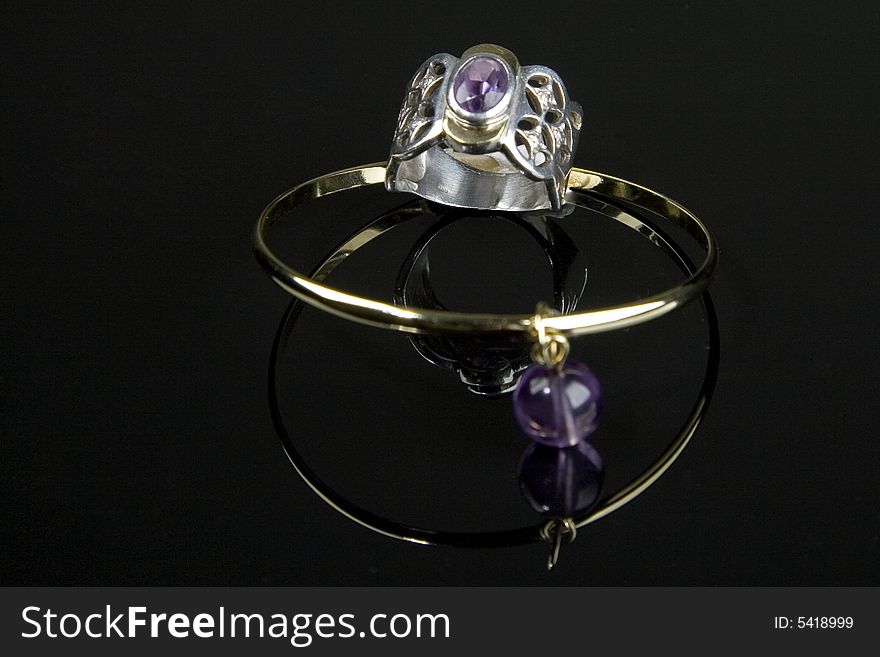 Gold ring and bracelet with amethyst reflected over black background. Gold ring and bracelet with amethyst reflected over black background