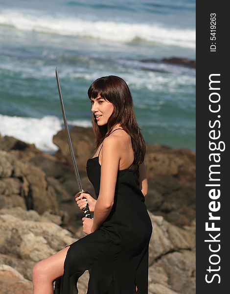 A beautiful white caucasian woman with a sword on the beach. A beautiful white caucasian woman with a sword on the beach