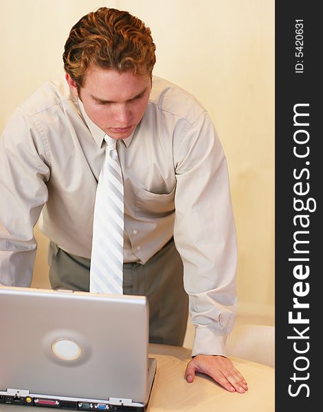 Front view of businessman in tan shirt standing over open laptop computer. Front view of businessman in tan shirt standing over open laptop computer